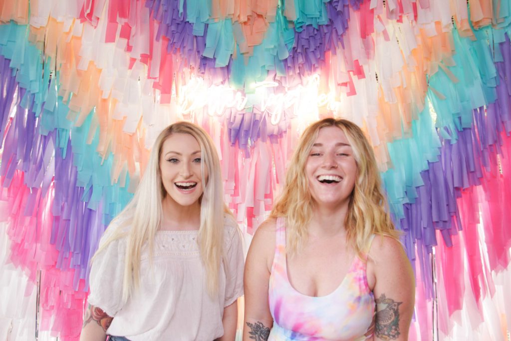 two girls smiling front of a colorful streamer backdrop