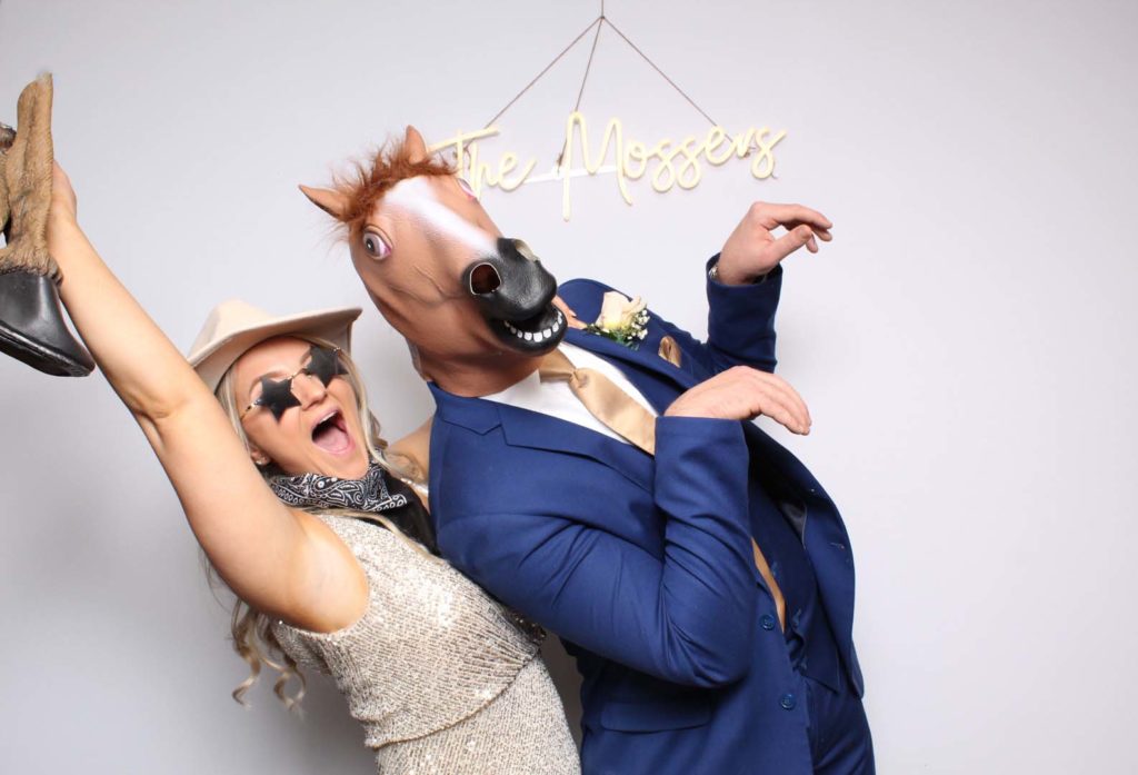 couple beign silly with a horse mask on ther face and some country hat
