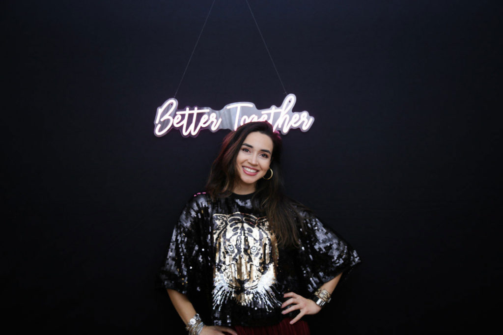 girl smiling front of a black backdrop with a pink neon sign behind