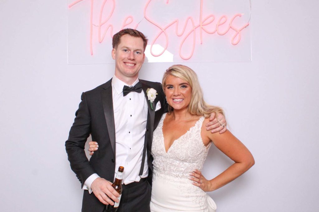 couple smiling with a custom neon sign in pink in. a white backdrop
